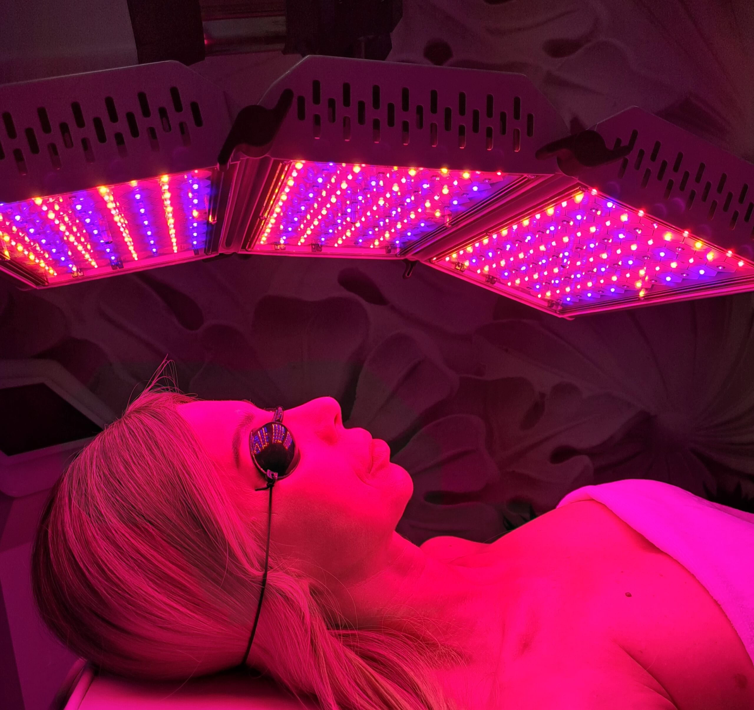 Kobieta leżąca w gabinecie podczas zabiegu z wykorzystaniem lampy LED, która świeci różowym kolorem